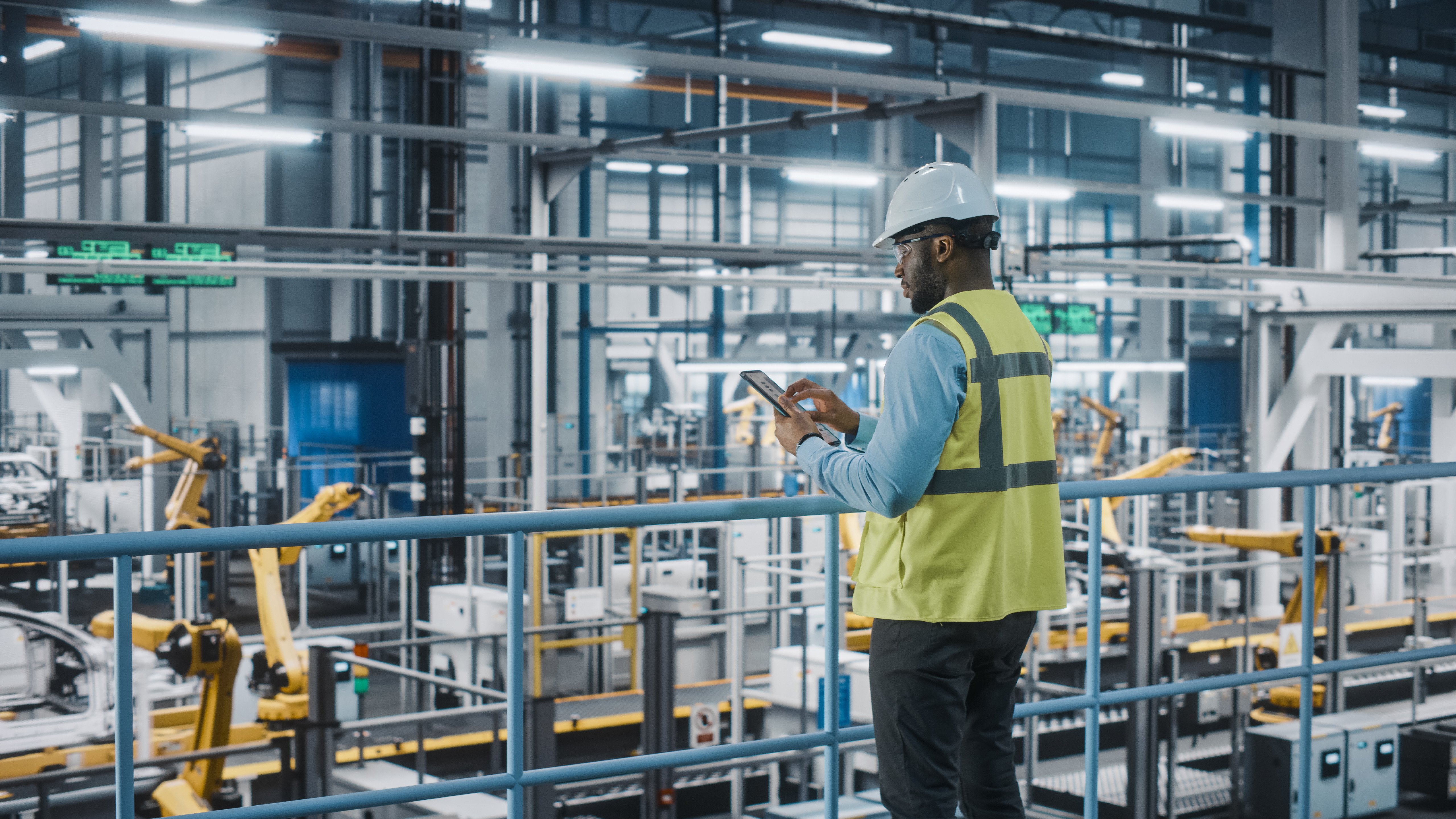 Male worker in safety vest and hard hat using tablet in a high-tech manufacturing facility