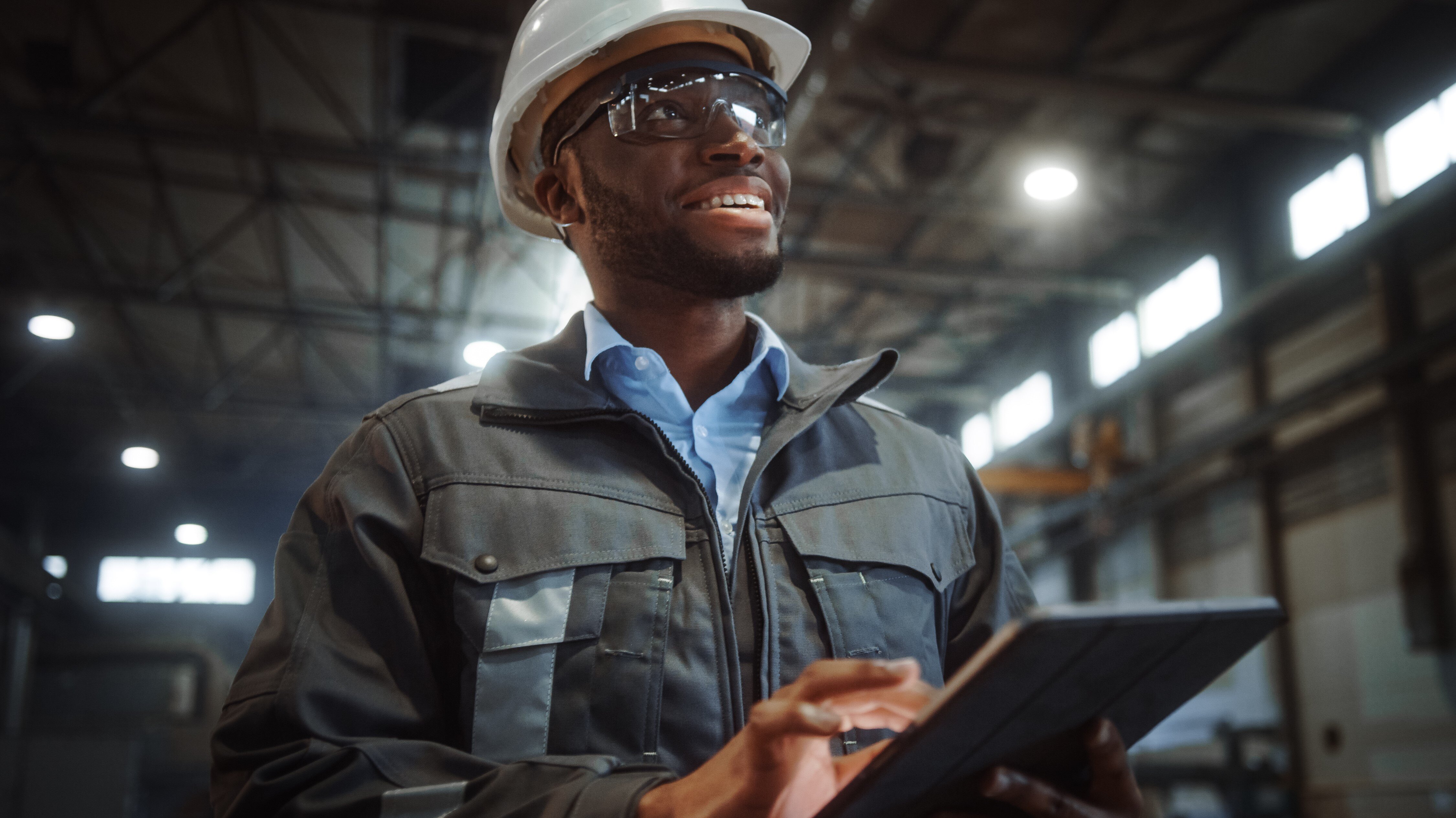 manufacturing worker with a hard hat smiling as he operates a tablet