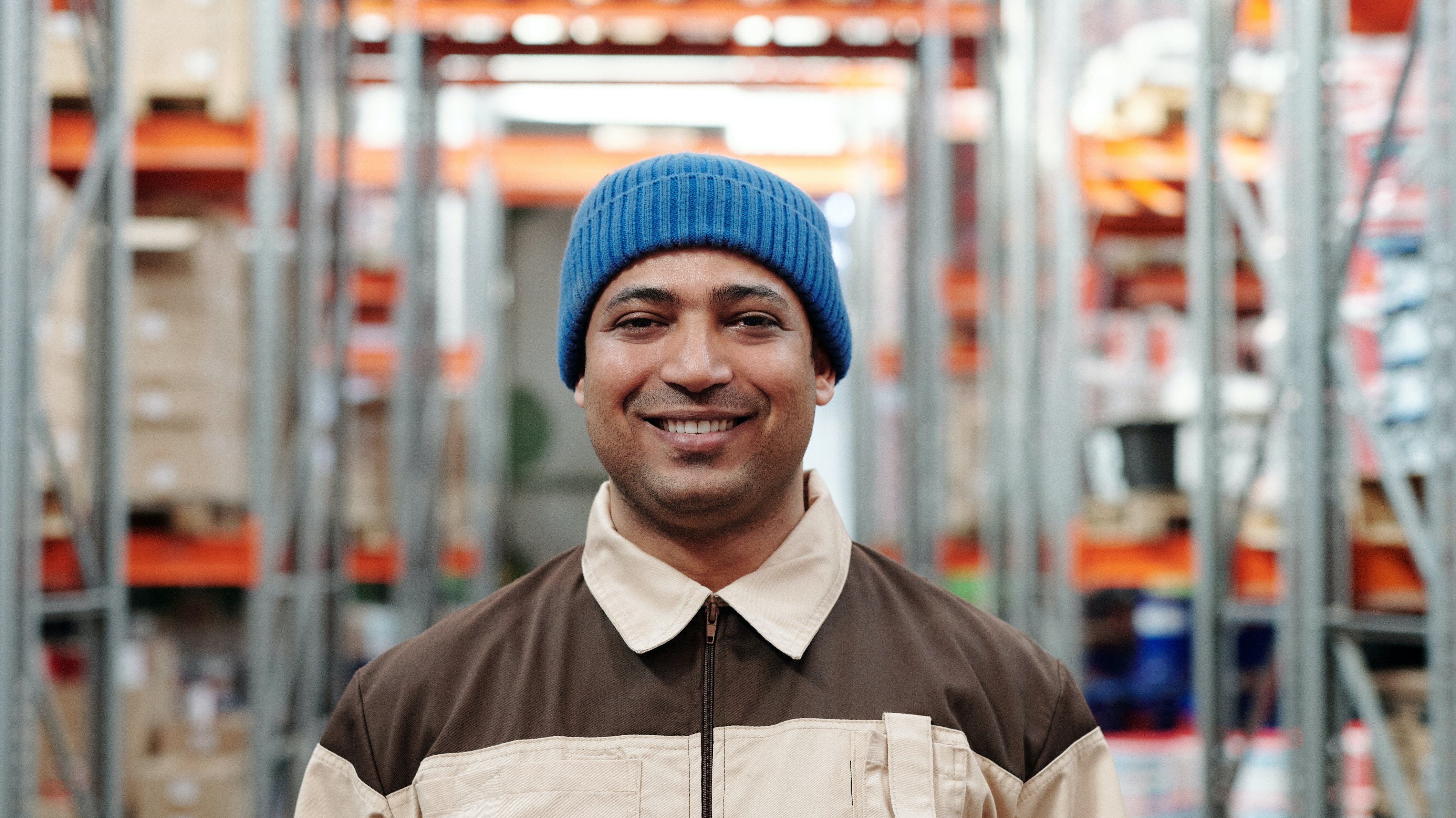 warehouse worker with work jumpsuit and blue beanie in between shelves in a warehouse